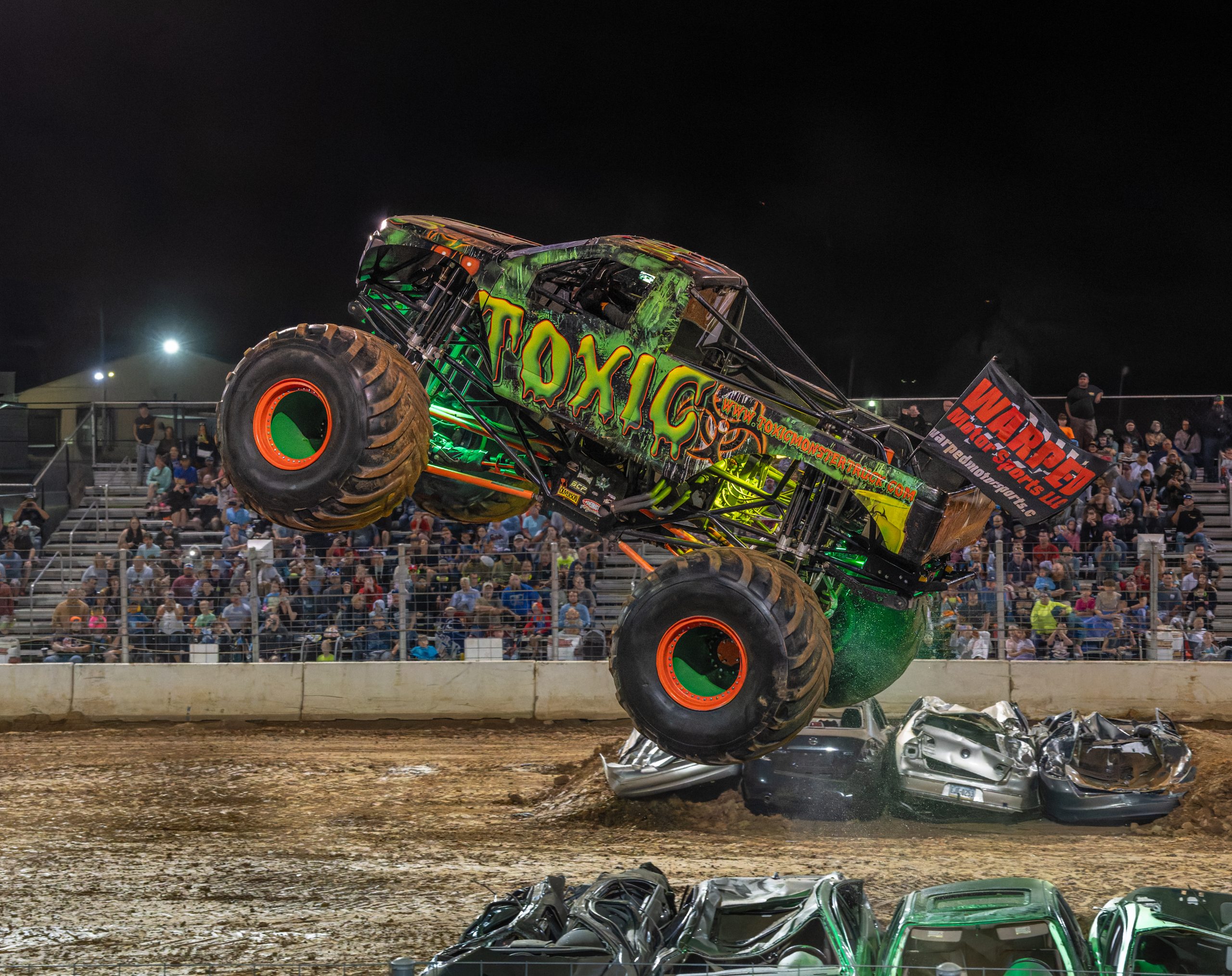 Toxic Monster Truck performing a big jump and crushing junk cars during the freestyle competittion